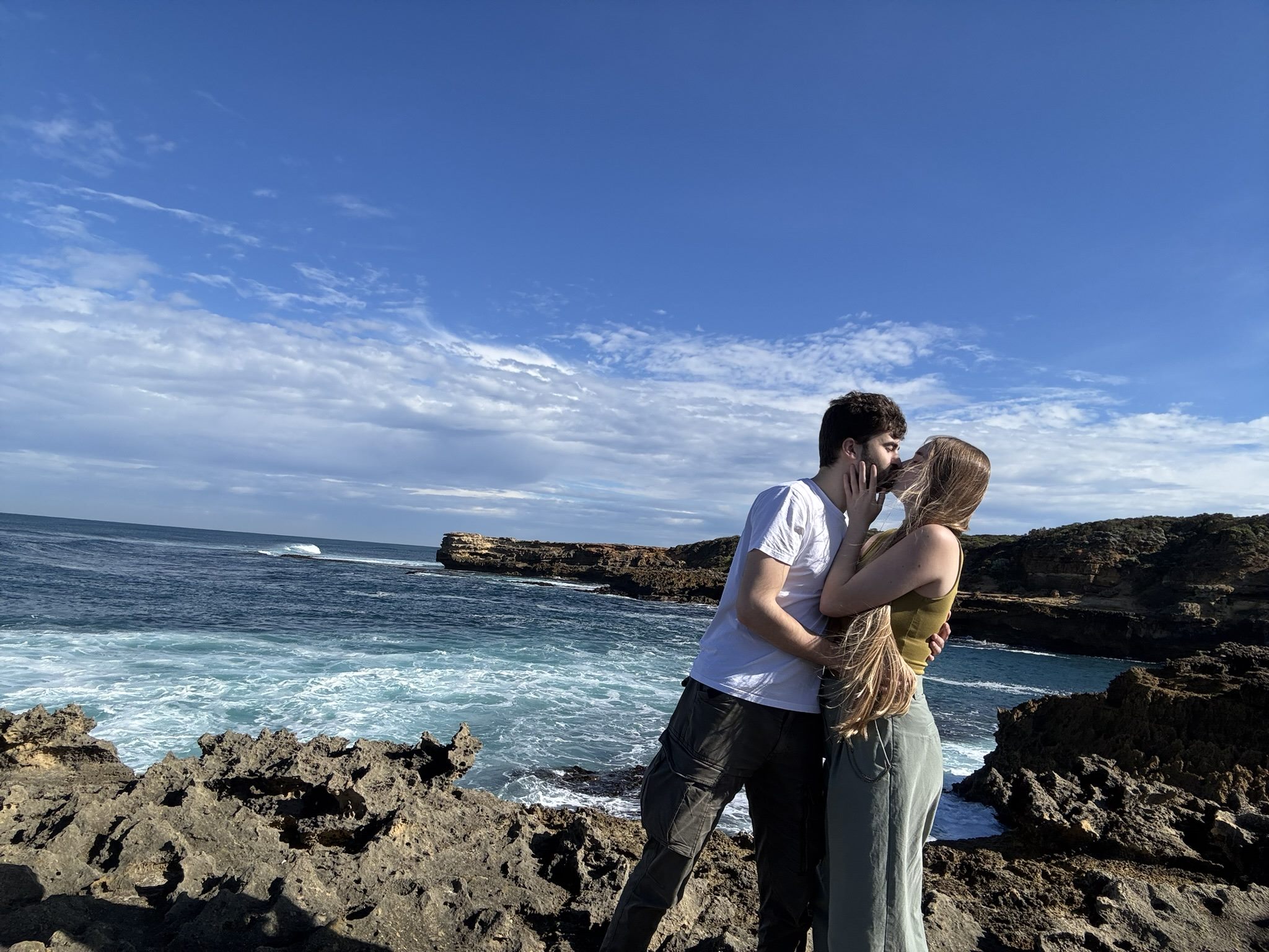 Callum and Celina kissing on the rocks above the sea