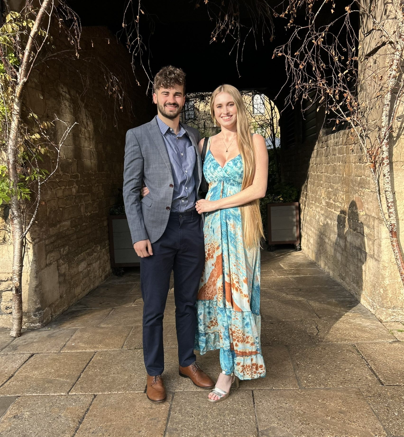 Callum and Celina dressed for a wedding under a stone archway