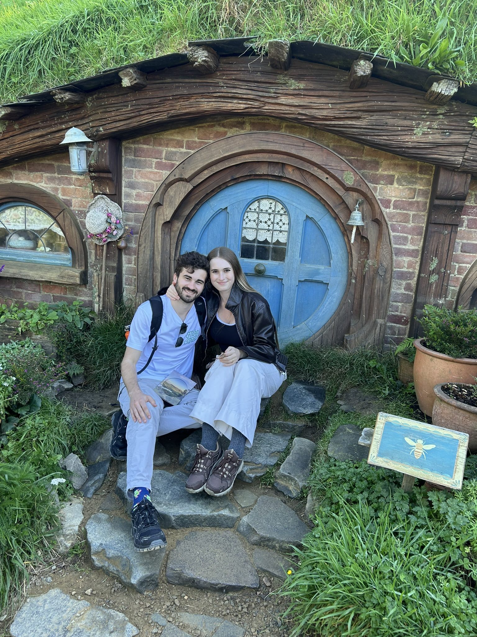 Callum and Celina on the step of a round door at Hobbiton