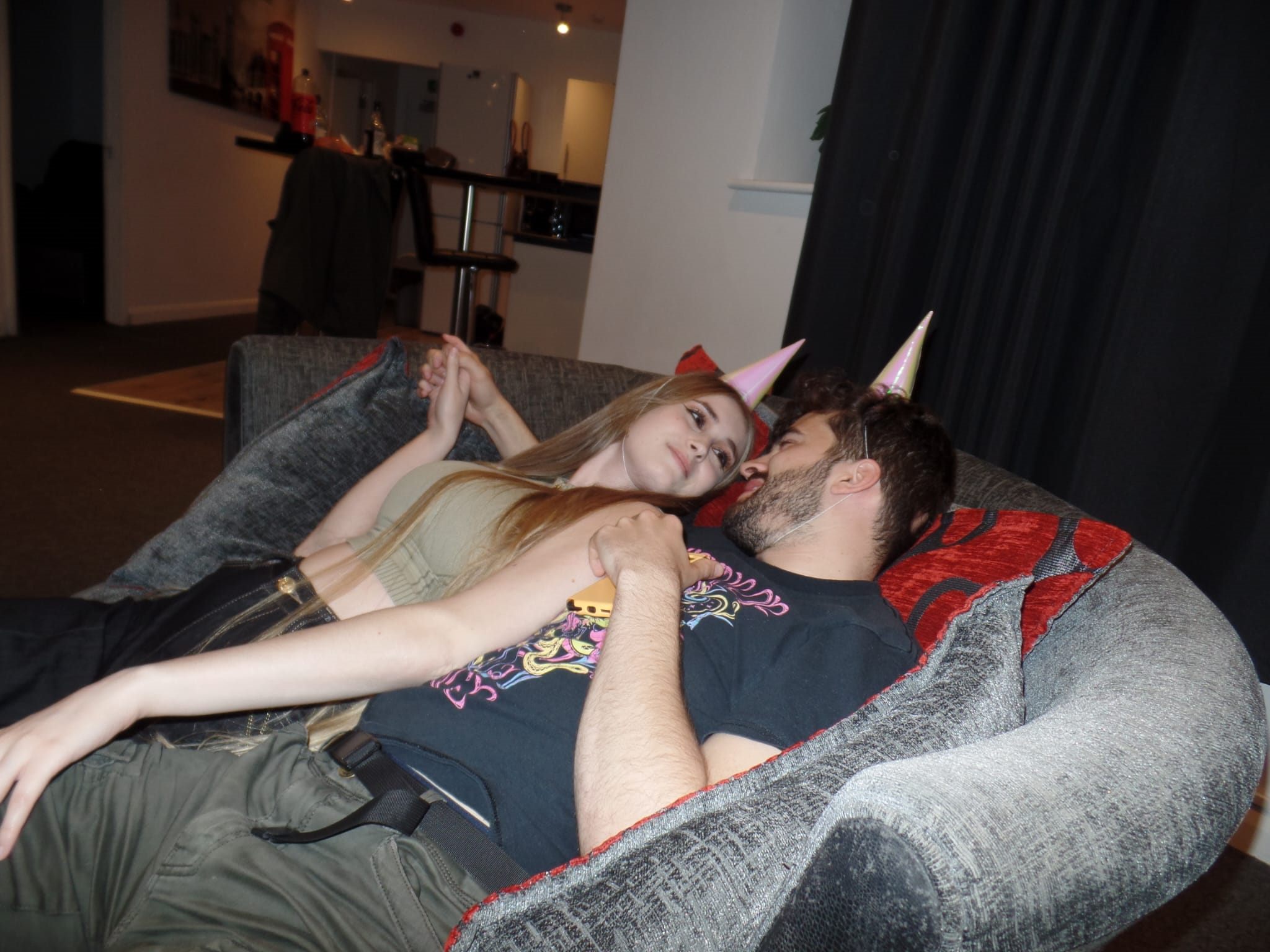 Callum and Celina in party hats on a sofa